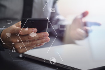 close up of businessman working with mobile phone and laptop computer on wooden desk in modern office with virtual reality icon diagram