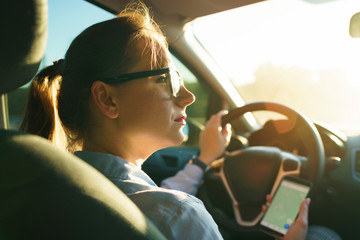 Happy woman uses a navigator in a smartphone while driving a car