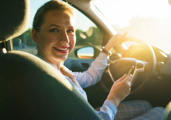 Happy woman uses a navigator in a smartphone while driving a car