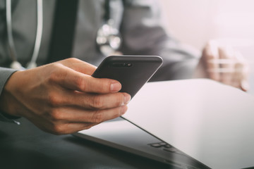 close up of smart medical doctor working with mobile phone and laptop computer and stethoscope on dark wooden desk
