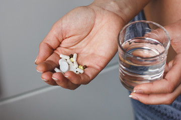 Many pills and drugs in woman hand. She is holding a glass of water. Doctor adviced a pills