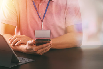 businessman in pink t-shirt working with smart phone and digitl tablet computer on wooden desk in modern office with glass reflected view