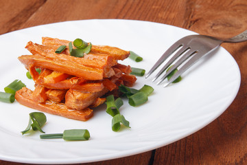 Baked carrots with green onions on a white plate. Organic Vegetarian Food on wooden background
