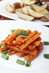 Baked carrots and potatoes with green onions on a white plate. Organic Vegetarian Food on a wooden background