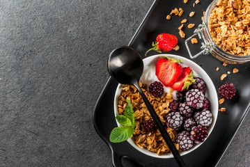 Healthy breakfast. Summer berries and fruits. Homemade Greek yogurt with granola, blackberries, strawberries and mint. On a black stone table, with the ingredients. Top view copy space