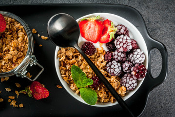 Healthy breakfast. Summer berries and fruits. Homemade Greek yogurt with granola, blackberries, strawberries and mint. On a black stone table, with the ingredients. Top view copy space