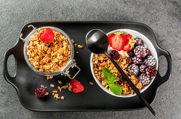 Healthy breakfast. Summer berries and fruits. Homemade Greek yogurt with granola, blackberries, strawberries and mint. On a black stone table, with the ingredients. Top view copy space