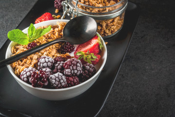 Healthy breakfast. Summer berries and fruits. Homemade Greek yogurt with granola, blackberries, strawberries and mint. On a black stone table, with the ingredients. Copy space