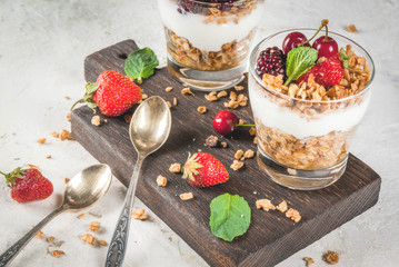 Healthy breakfast. Summer berries and fruits. Homemade Greek yoghurt with granola, blackberries, strawberries, cherries and mint. On white concrete stone table, in glasses. Copy space