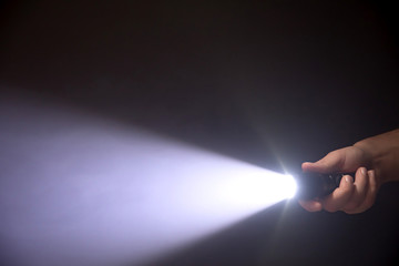 Black flashlight a beam of light directed at the viewer in male's hand isolated from right side of the frame on black background