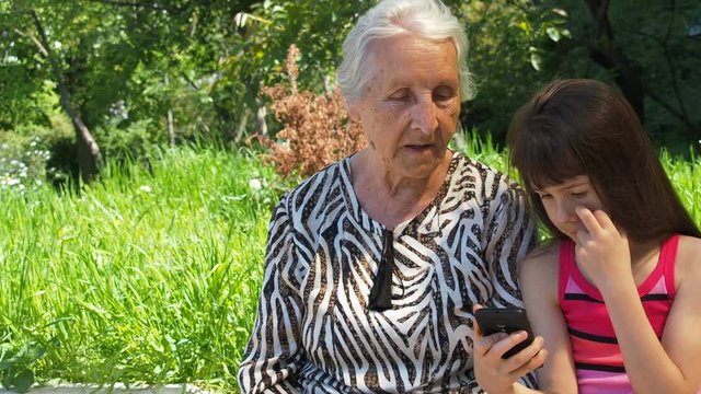 Grandmother with granddaughter. Granddaughter shows grandmother a mobile phone. Family with mobile phone in nature.