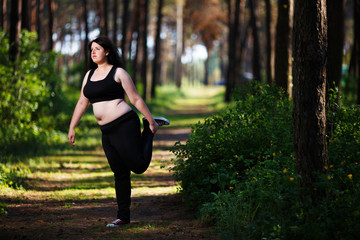Young overweight woman stretching legs in the park