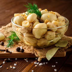 Pickled mushrooms in glass bowl with spices and dill on wooden table.