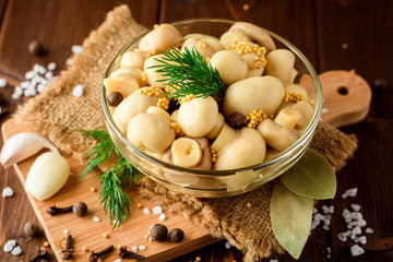 Pickled mushrooms in glass bowl with spices and dill on wooden table.