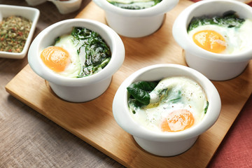 Bowls with tasty eggs and spinach on wooden table