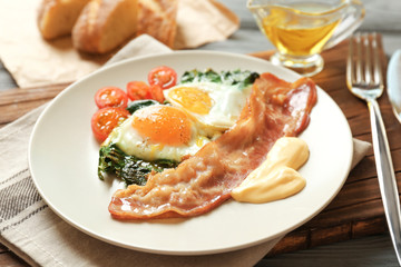 Plate with tasty eggs, spinach and bacon on wooden table