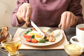 Woman eating tasty eggs, spinach and bacon on table