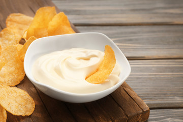Bowl with tasty mayonnaise sauce and chips on wooden table, closeup