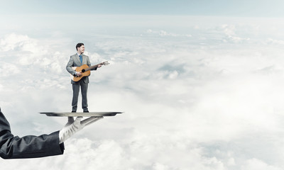 Fototapeta na wymiar Businessman on metal tray playing acoustic guitar against blue sky background