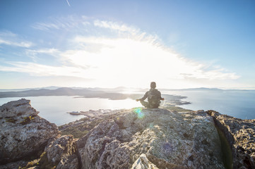 A traveler is doing yoga on the top of the mountain at sunset in Sardinia, Italy.