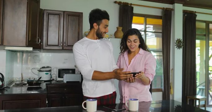 Couple Using Cell Smart Phone In Kitchen Laugh Talking, Young Man And Woman Morning Communication Slow Motion 60