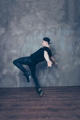 Fototapeta na wymiar Young modern dancer is posing on a studio background while dancing. He is in black outfit