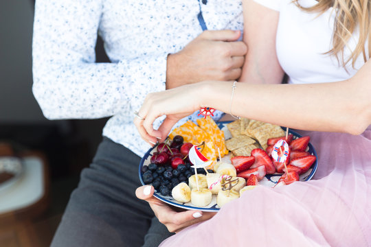 Plate with fruit and snack. Cheese, cracers, cherry, strawberry, blueberry, banana, snakcs. Nautical toothpicks. Plate on the couple hand, hands