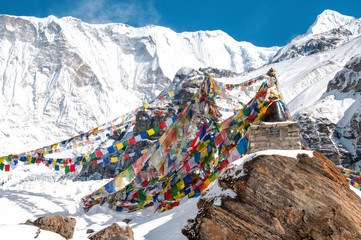 Buddyjskie flagi modlitewne w Annapurna Base Camp i ośnieżone góry w tle. 