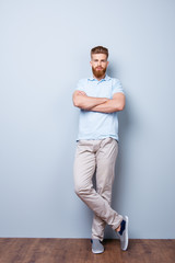 Success concept. Confident handsome red bearded young man in casual stylish outfit, standing on the pure background, his hands and legs are crossed