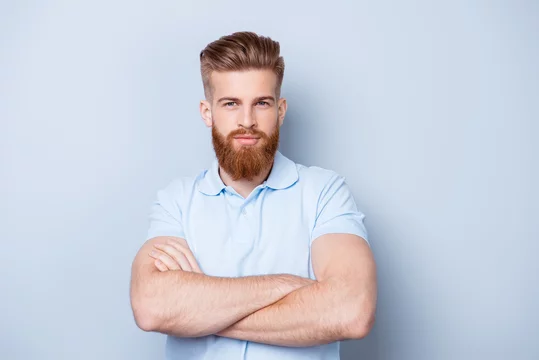 Barbershop advertising. Close up portrait of severe hot red bearded guy with stylish hairdo. He is standing with crossed arms on pure background, in casual light t shirt