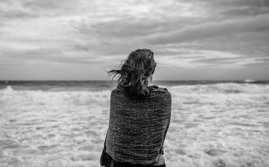 Young woman wrapped in scarf on the beach rear view