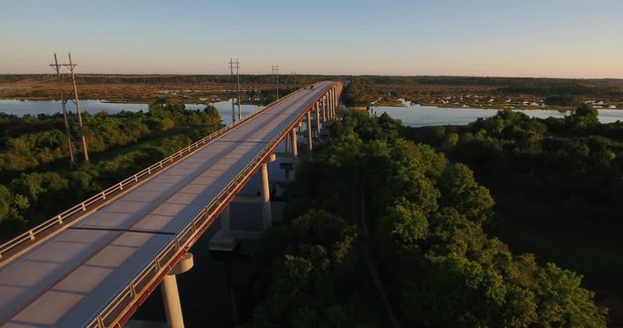 An early morning sunrise low moving forward aerial establishing shot of the Topsail Island Bridge over the Intracoastal Waterway as traffic passes over top.  	