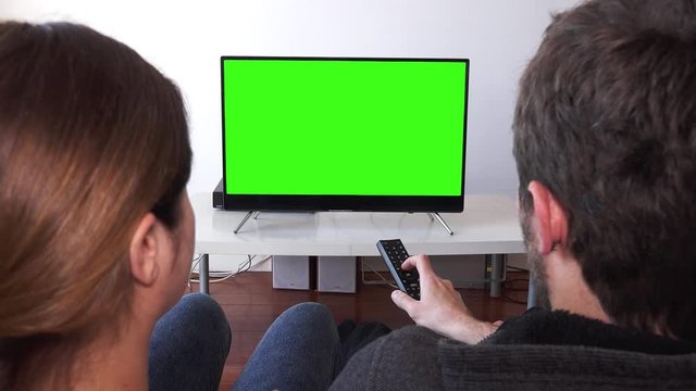 Couple Changing Channels On Green Screen Television. Couple watching television with green screen. Shot behind models shoulders