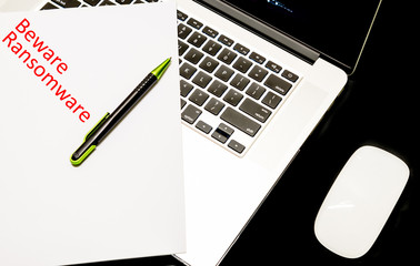 Close-up handwriting word beware ransomware on white paper over laptop with map of global ransomware cyber attack background. Cyber security concept.