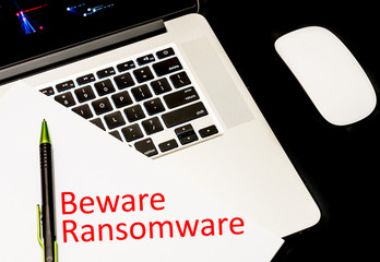Close-up handwriting word beware ransomware on white paper over laptop with map of global ransomware cyber attack background. Cyber security concept.