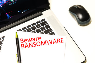 Close-up handwriting word beware ransomware on white paper over laptop with map of global ransomware cyber attack background. Cyber security concept.