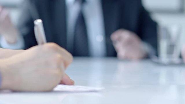 Closeup shot of hands of businesswoman signing document while her colleague explaining something at meeting