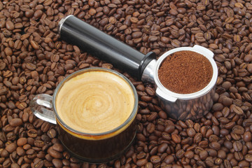 Cup of hot coffee with ground coffee in espresso machine portafilter on roasted