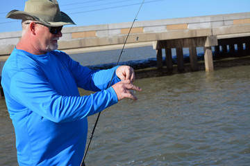 Fishing Blue Shirt/Angler standing near body of water removing small fish from fishing line