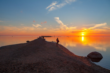 Fototapeta na wymiar Colorful sunset over sand coast of the sea. Woman enjoying dawn