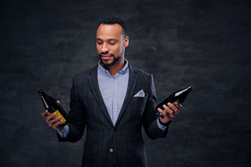 Studio portrait of elegant black male in a suit holds beer bottles.