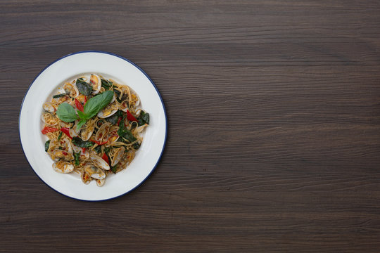 Stir fried Clams and Spaghetti with chili paste in the white dish on brown wooden table / Selective focus, space for text.