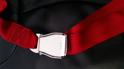 Seat belt on seat shot in airplane with Black seat and red carpet.