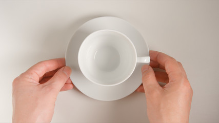 TOP VIEW: Human hands puts a white teacup on a white table