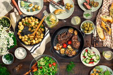 Dinner table with meat grill, roast new potatoes, different food - Powered by Adobe