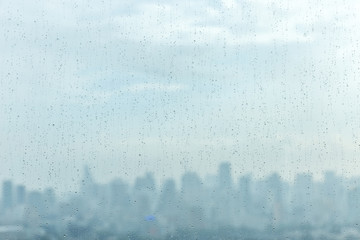 Rain drops on window glass and blurred cityscape and sunlight in background.