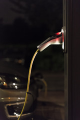 View of an Electric Car Charging Column at night and in the background a partial view of a car