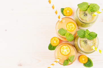 Freshly blended orange kumquat and green kiwi fruit smoothie in glass jars with straw, mint leaf,...