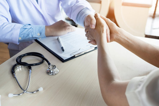 Doctor shakes hands at medical office with patient, wearing glasses, stethoscope and lab coat.