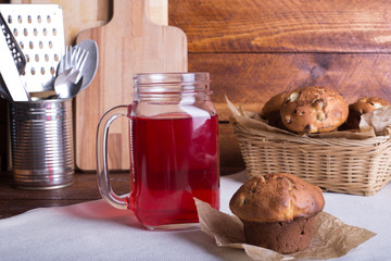 Fresh and healthy red Fruit juice drink  in a glass and jug and muffin or cake in the in a wicker basket on the wooden brown table background. Side view.